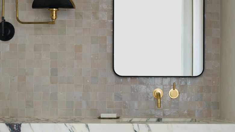 Pirinç musluk ve aydınlatma armatürü bulunan makyaj masasının üzerinde beyaz zellige karo backsplash.