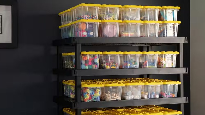 Siyah plastik raf ünitesinde istiflenmiş Sarı Kapaklı HDX 6,5 Qt Sert Şeffaf Saklama Kutusu