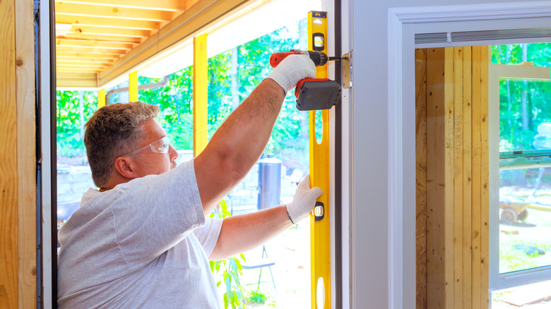 Bir adam kapısının düzgün bir şekilde açılmasını sağlamak için bir seviye kullanıyor