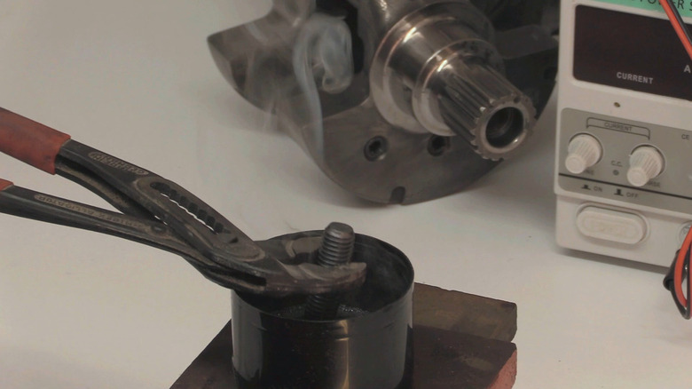 bir kişi ısıtılmış cıvatayı bir bardak yağa batırır