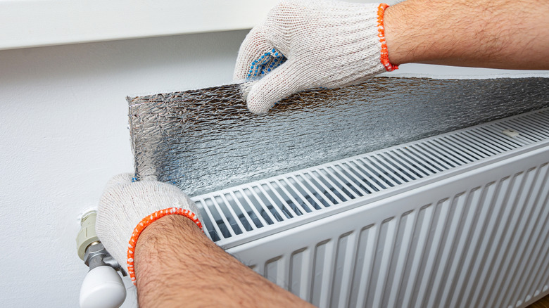 Eldivenli eller alüminyum folyoyu radyatörün arkasına yerleştiriyor.