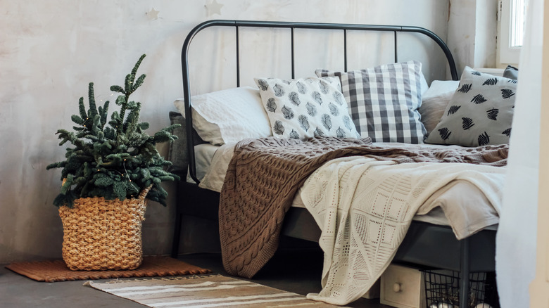 Örme battaniyeler ve bir ev bitkisinin bulunduğu pencerenin yanında bir yatak.