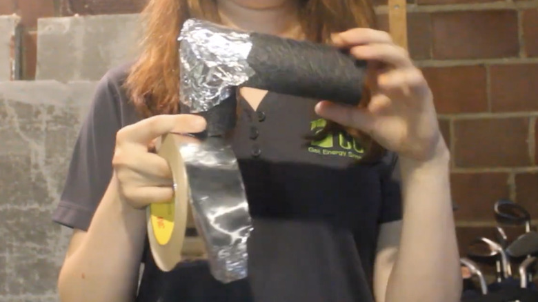 Bir kadın köpük boru yalıtımının etrafına alüminyum folyo bant sarıyor.