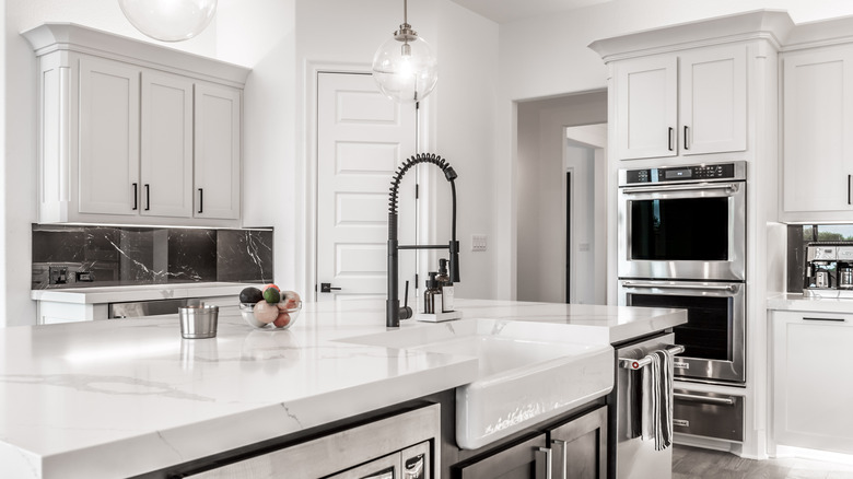 Paslanmaz çelik aletler, beyaz tezgahlar, beyaz duvarlar ve beyaz dolaplarla donatılmış modern mutfak