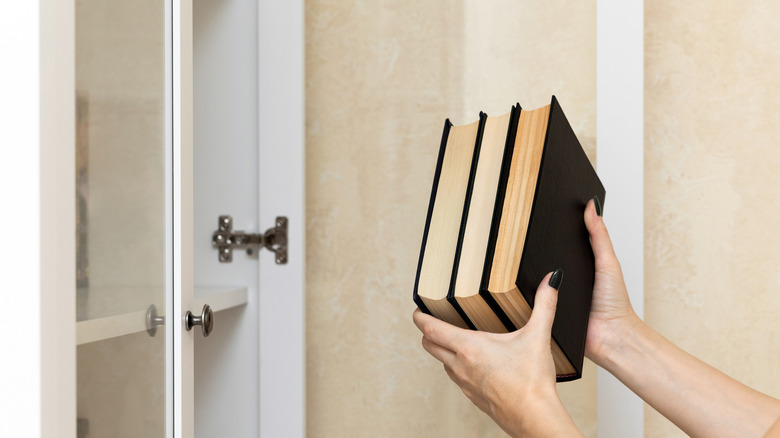 Bir kadın bir çin dolabının yanında bir yığın kitap tutuyor