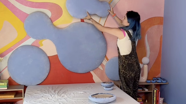 Bir kişi yatağın üzerine mavi kadife çok parçalı bir yatak başlığı monte ediyor.