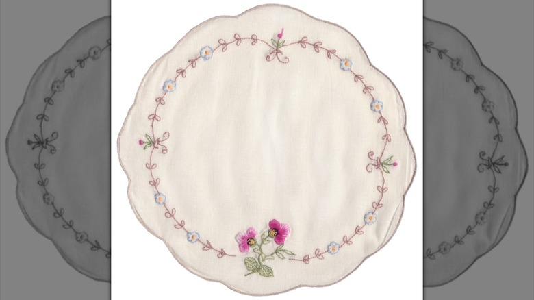 Beyaz zemin üzerine fistolu, yuvarlak, işlemeli bir bardak altlığı peçete.