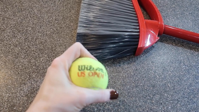 Siyah ve gri kıllı kırmızı bir süpürgenin önünde Wilson ABD Açık tenis topu tutan el