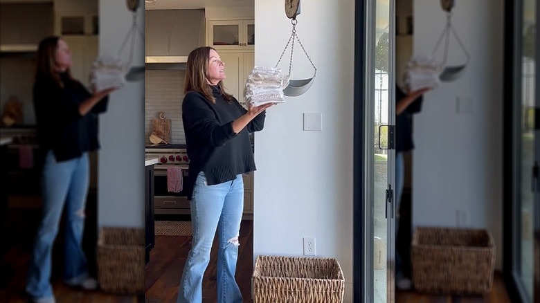 Mutfak havlularını eski bir teraziye, altına da kirli bir çamaşır sepeti koyan bir kişi