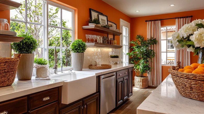 Koyu renkli ahşap dolaplar, doğal taş tezgahlar ve cam, hasır ve bitki desenli yanık turuncu duvarlara sahip modern mutfak