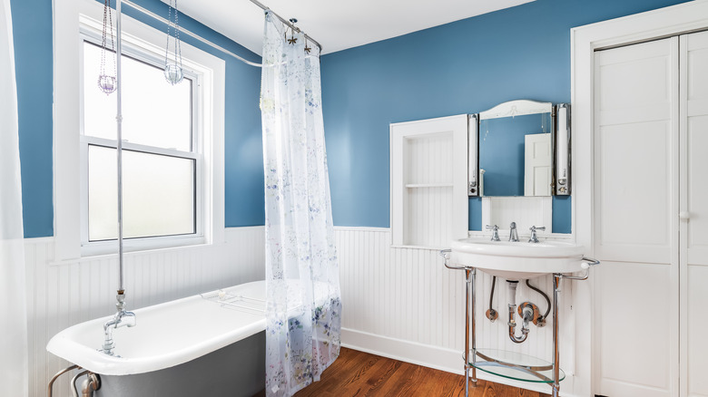 Mavi beyaz banyoda şeffaf perdeli pençe ayaklı küvet