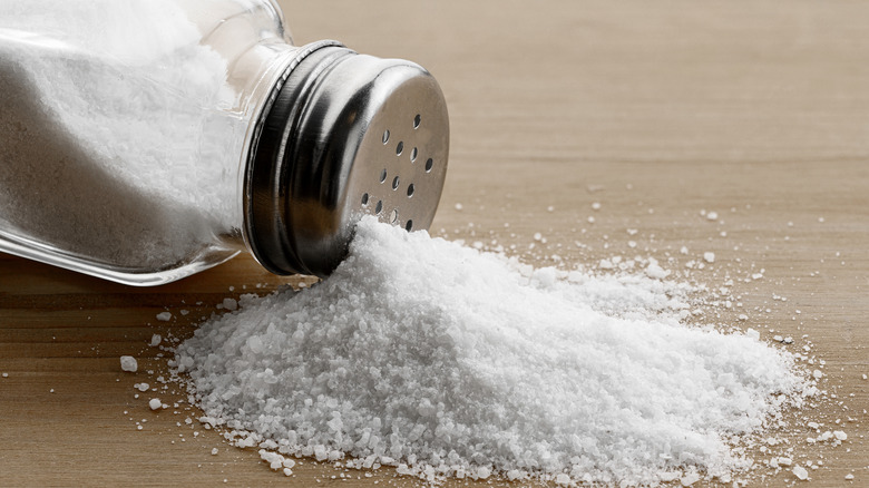 Tuz, cam ve metal tuzluktan ahşap bir masanın üzerine dökülüyor.
