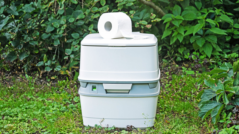 Ağaçların ve bitkilerin önünde, üstünde tuvalet kağıdı olan kompost tuvalet