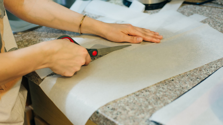 Bir çift el, mumlu kağıt parçalarını makasla kesti.