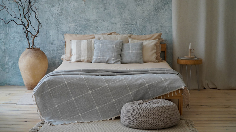 Birden fazla yastıklı yatak, mumlu yuvarlak komidin ve yan taraftaki vazoda kurutulmuş dallar.