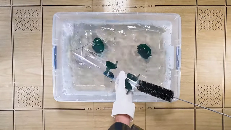 Eldivenli elleri olan kişi kuş besleyicisini plastik bir küvetin içindeki sabun ve su solüsyonunda temizliyor