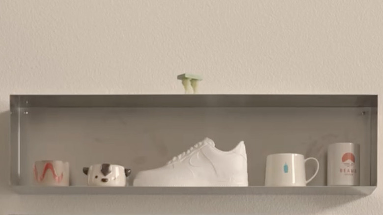 Duvara monte edilmiş ve kupa gibi dekor öğeleriyle kaplı metal saksı