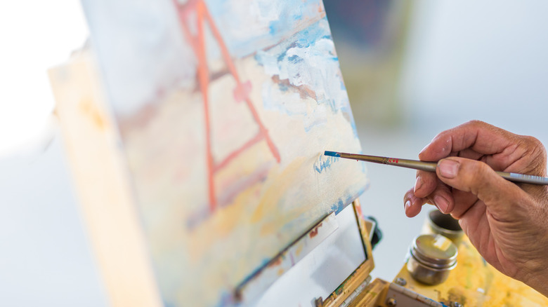 Bir sanatçı, resmini bir fırçayla imzalıyor.