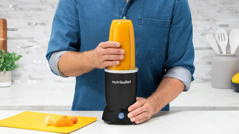 Portakalları karıştırmak için nutribullet karıştırıcı kullanan bir adam.