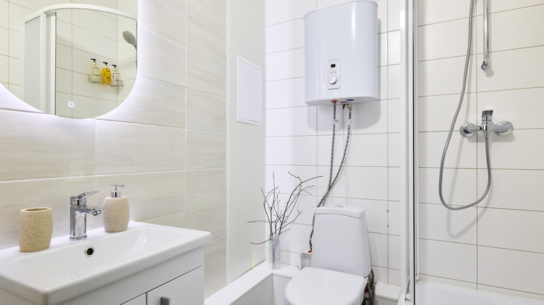 Tuvalet üstü tankı, küçük bir duşu ve ışıklı aynası olan bir banyo