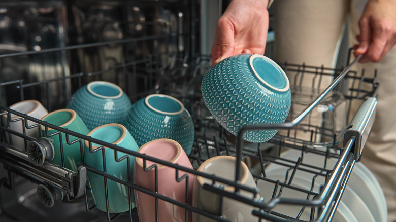 Eller seramik kaseleri ve fincanları bulaşık makinesinin üst rafına yerleştiriyor.