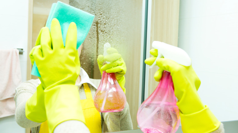 Banyo aynasını sünger ve sirke solüsyonuyla temizleyen kişi.