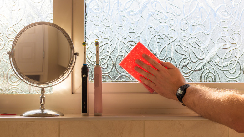 Banyodaki cam pencereyi temizleyen kişi.