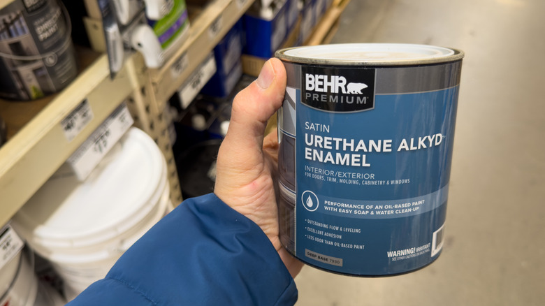 Bir mağazada üretan emaye boya kutusu tutan bir kişi