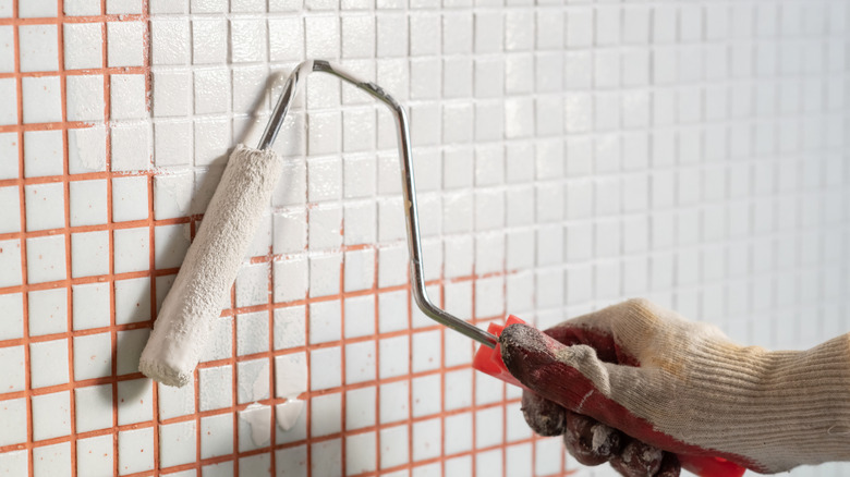 Kiremitli bir duvarı turuncu harçla boyamak için beyaz boya kaplı rulo kullanan bir kişi