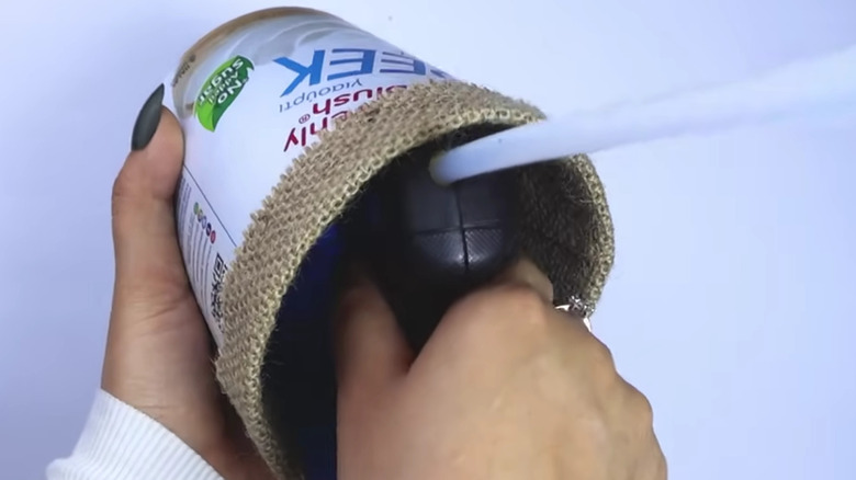 Bir kadın yoğurt kabının üstüne çuval bezi sarıyor ve yapıştırıyor