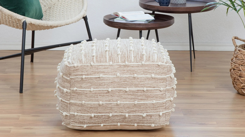 Yatak odasında beyaz bir dolap ve çiçekliklerin yanında yere açık kırmızı bir puf yerleştirilmiştir.