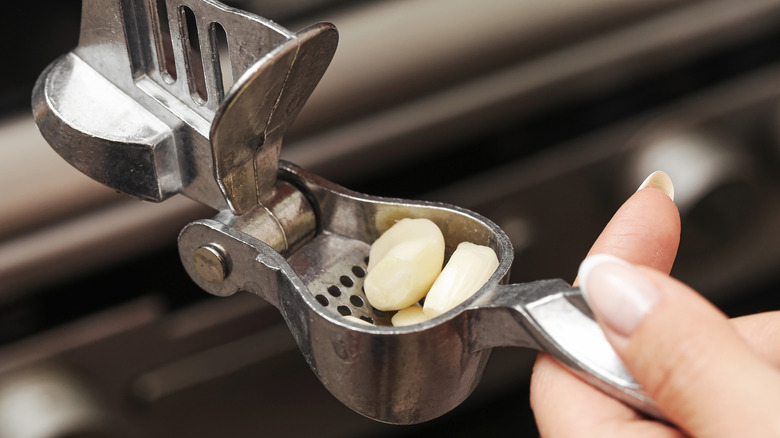 İçinde sarımsak karanfilleri olan bir sarımsak presini tutan eller