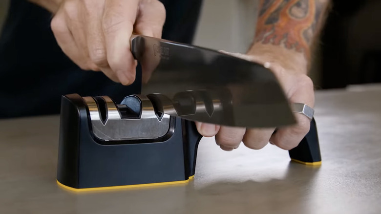 Bir şef, içinden geçmeli bıçak bileyici kullanarak bıçağını keskinleştiriyor