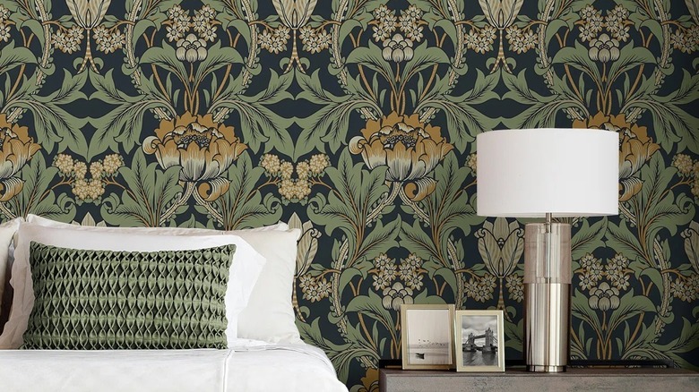 Beyaz çarşaflı bir yatağın, bir lambanın ve yeşil çiçekli vintage tarzı duvar kağıdının bulunduğu bir yatak odası