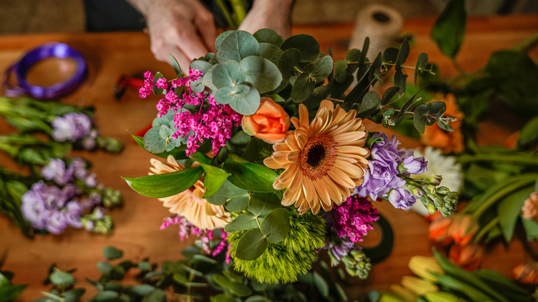 Kişinin elleri karışık çiçek ve yeşilliklerden oluşan bir demet düzenliyor.