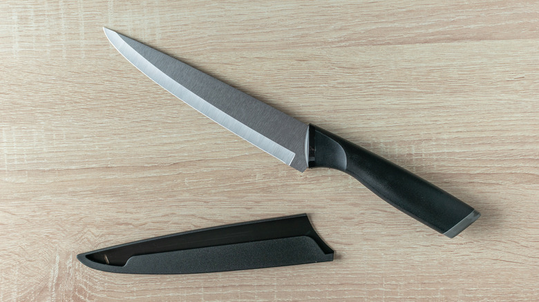 Bir şef bıçağı, kılıfın yanındaki ahşap tezgahın üzerinde duruyor.