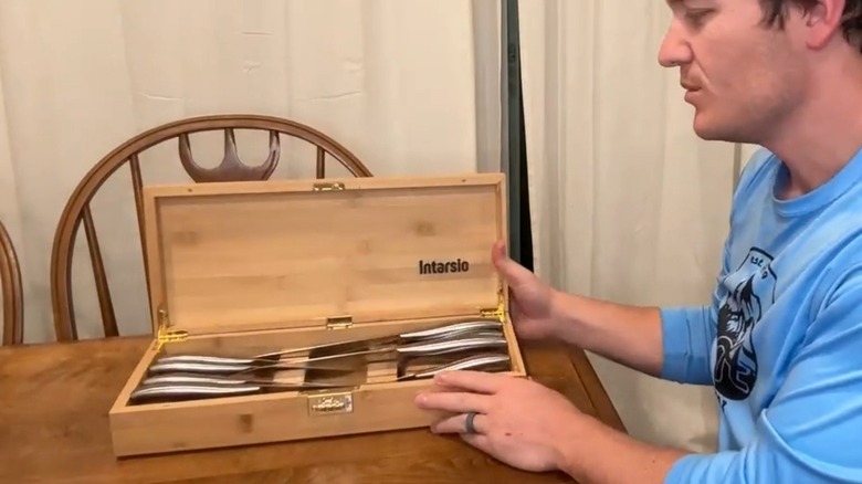 Ahşap bir masanın üzerinde kilitli bıçak kutusunu gösteren bir kişi