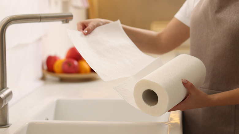 Bir kişi mutfak lavabosunun yanında dururken rulodan kağıt havlu çekiyor.