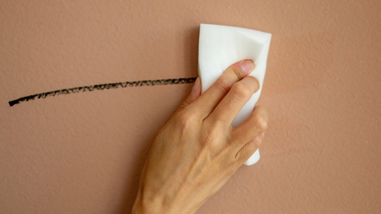 Yakın çekim fotoğrafta boyalı duvardaki izi melamin köpük süngerle temizleyen bir el görülüyor