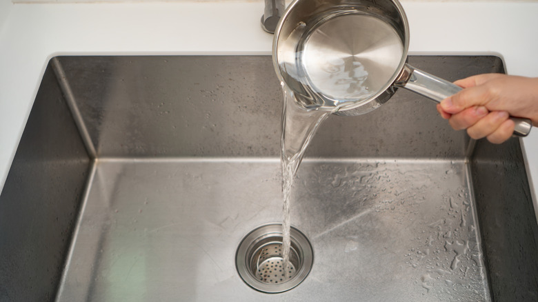 paslanmaz çelik bir tencereden mutfak giderine kaynar su döken el