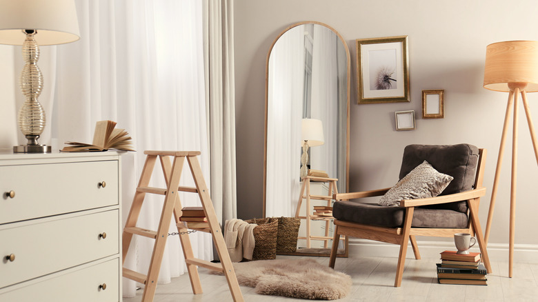 Merdiven, lambalar, şifonyer, kahverengi yastıklı sandalye ve duvara yaslanmış kemerli ayna ile ışık odasının içi