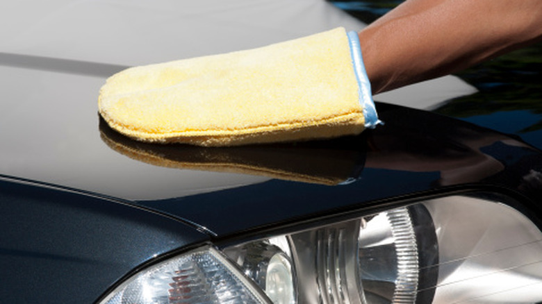 Bir kişi elindeki bez eldiveni kullanarak arabayı parlatıyor