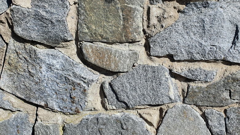 Yakın plan fotoğraf, istinat duvarındaki tarla taşının eşit olmayan boyutlarını ve dokularını gösteriyor