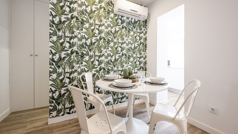 Yemek takımının arkasında tropikal duvar kağıdına sahip küçük bir yemek odası.