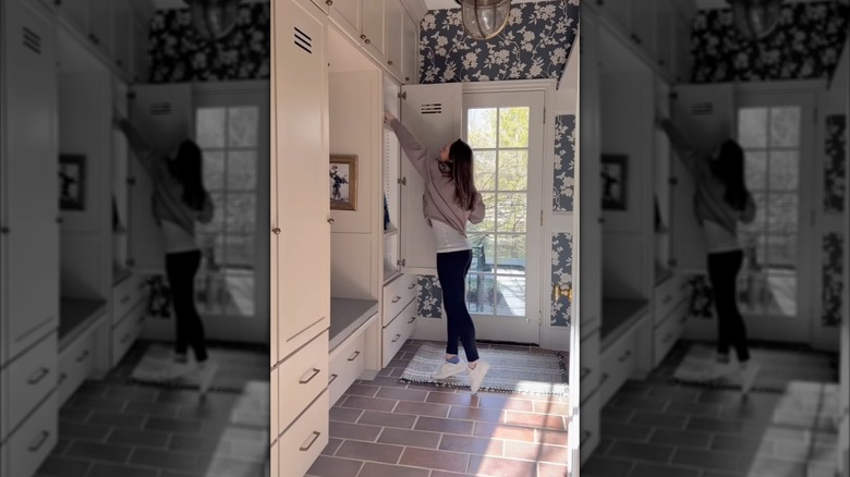 Duvar kağıdıyla kaplı çamur odasında ayakkabılarını kaldıran bir kadın.