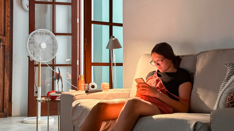 Stratejik olarak yerleştirilmiş bir fan, loş bir odada kanepede oturan bir kişiyi işaret ediyor