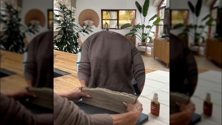 Bir kadın yuvarlak bir IKEA aynasının her iki tarafına iki traverten levha yapıştırıyor.