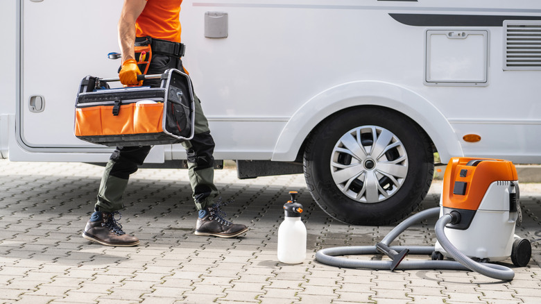 Dışarıda elektrikli süpürge ve temizlik şişesi olan bir çanta taşıyan adam