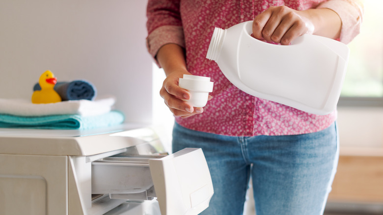 Bir kadın şişe kapağına bir ölçü çamaşır deterjanı döküyor.