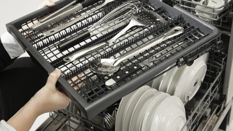 Bulaşık makinesinden kap tepsisini çıkaran bir kişi